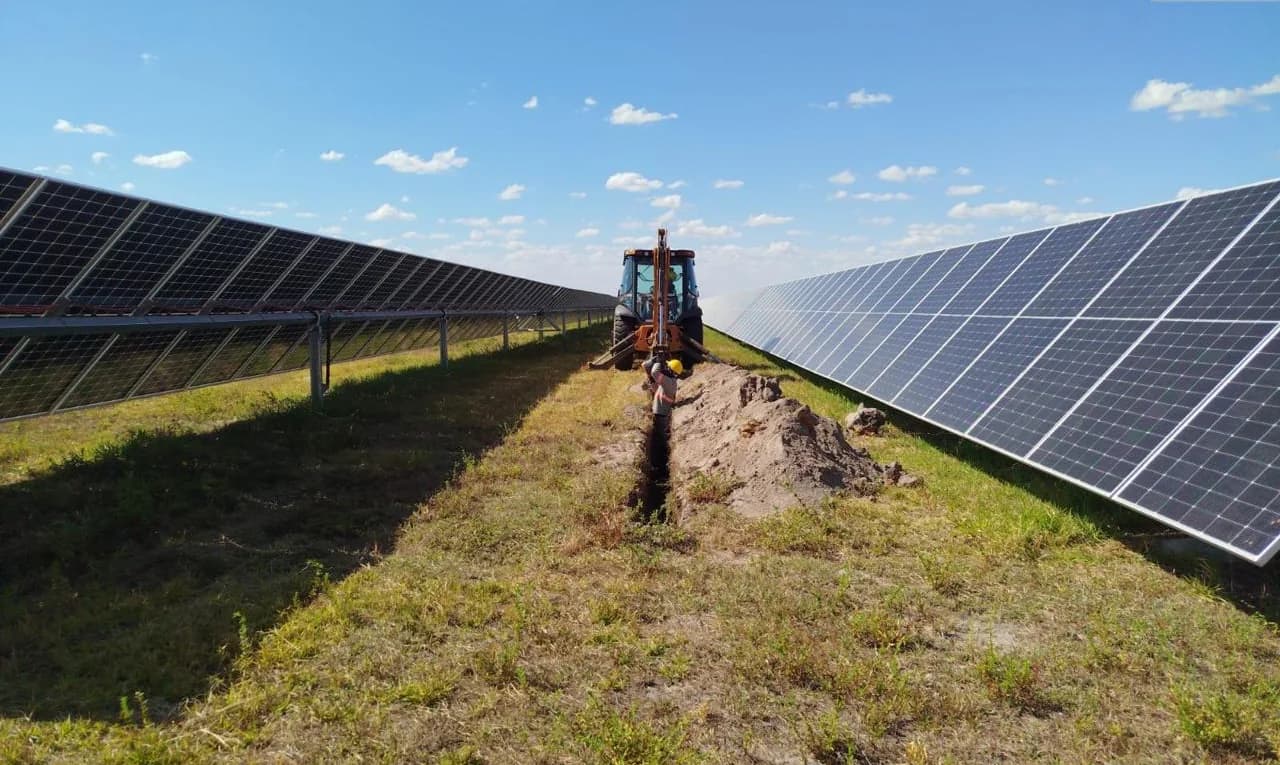 Retroescavadeira abrindo vala entre fileiras de módulos fotovoltaicos